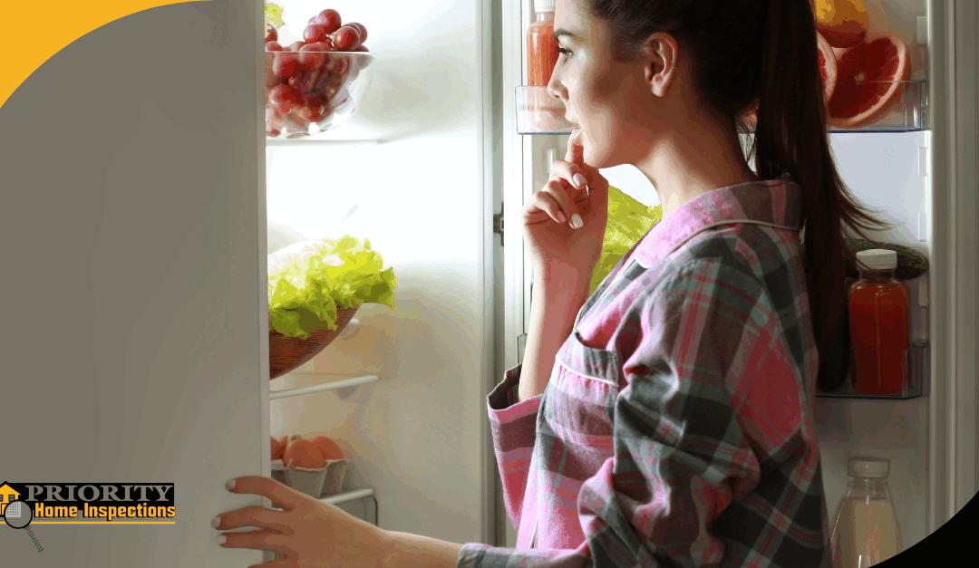 Woman in pajamas looking into a refrigerator filled with fruits and vegetables.
